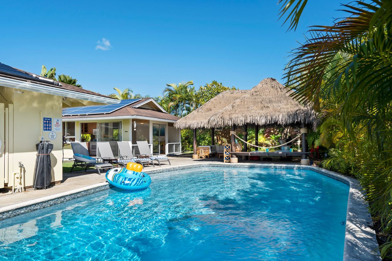 A serene tropical getaway featuring a swimming pool surrounded by lush greenery and thatched shade.